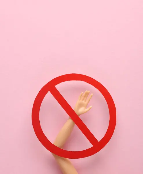 Doll hand with prohibition sign on pink background
