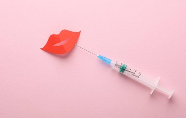 Dudak büyütme prosedürü. Kağıt dudaklar ve pembe arka planda bir şırınga. Yaratıcı düzen, güzellik konsepti