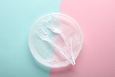Kırık plastik tabak, çatal ve kaşık pembe mavi arka planda. Plastik kirliliğini, geri dönüşümü, ekolojik konsepti durdurun. Üst görünüm