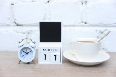 11 Ekim tarihli ahşap takvim ve tuğla duvar zemininde kahve fincanı olan çalar saat. Teslim tarihi, planlama, iş konsepti