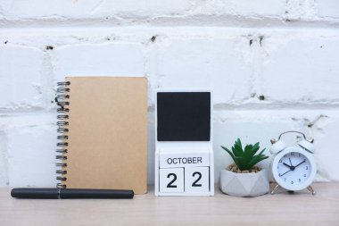 22 Ekim tarihli ahşap takvim, çalar saati olan defter ve tuğla duvar arka planına karşı masaya yerleştirilmiş. Teslim tarihi, planlama, iş konsepti