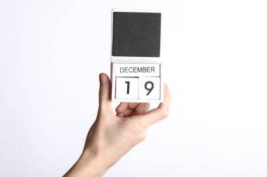 Beyaz arka planda 19 Aralık tarihli ahşap takvim tutan kadın.