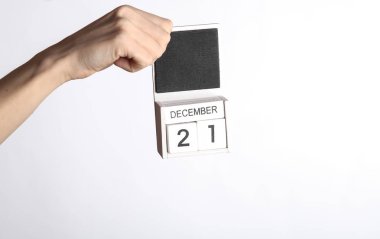 Beyaz arkaplanda 21 Aralık tarihli ahşap takvim tutan kadın.