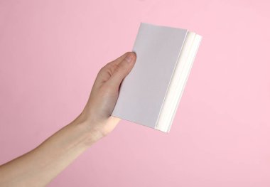 Kadın eli, pembe arka planda beyaz kapaklı kitabın maketini tutuyor. Tasarım şablonu
