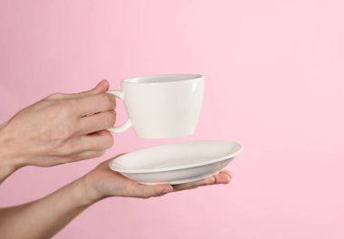 Kadın eli beyaz bir seramik bardak ile pembe arka planda bir fincan tutar.