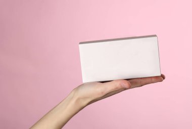 Pembe arka planda bir kadının avucundaki boş beyaz karton kutu.