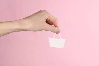 Kadının eli pembe arka planda kağıt kesikli süpermarket sepeti tutuyor..