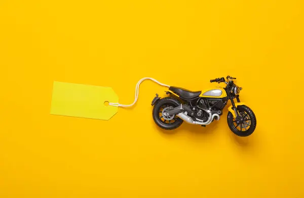 Toy motorbike model with price tag on yellow background. Top view
