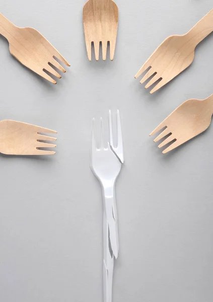 Broken plastic fork and wooden forks on a gray background. Plastic free, recycling, eco concept