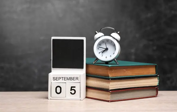Calendar with september 05 date and books with alarm clock on table against chalk board background
