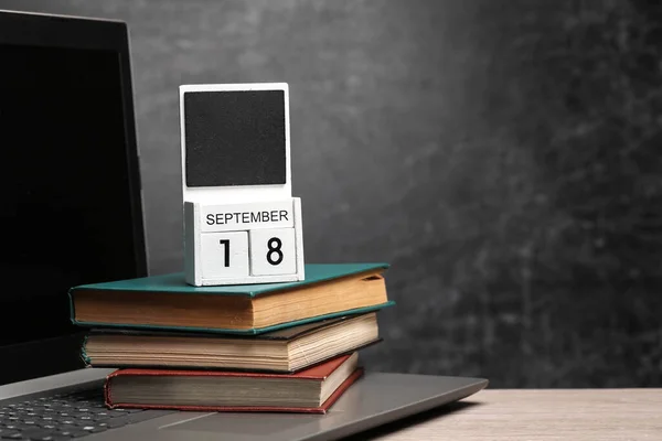 Calendar with september 18 date and laptop with books on table against chalk board background
