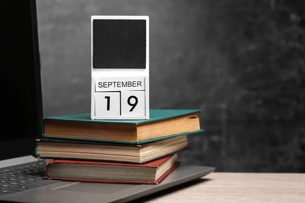 Calendar with september 19 date and laptop with books on table against chalk board background