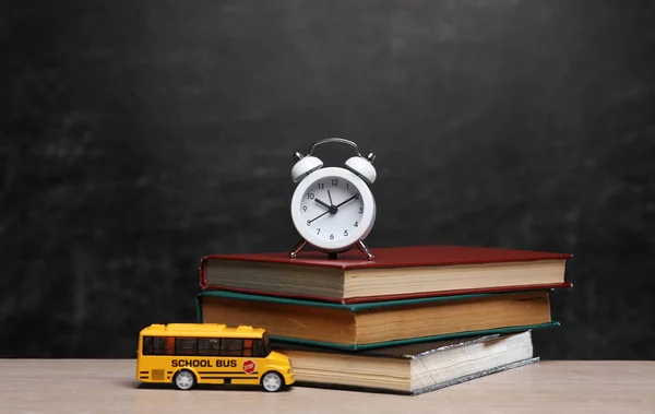 Miniature School bus with alarm clock and books on table against the background of chalkboard. Back to school