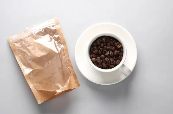 Ceramic coffee cup with coffee beans and packing package on gray background. Top view