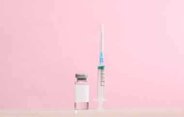 Pembe arka planda şırıngalı aşı şişesi.