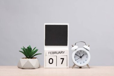 Aylık beyaz tahta blok takvimi, tarih Şubat 07 ve alarm saati, masaya yerleştirilmiş, gri arka plan. Planlama, iş konsepti