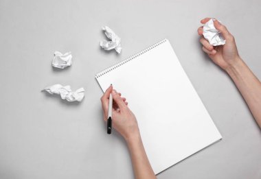 Fikir yoksunluğu. Kadın elleri eskiz defterinde biseksüeldir ve gri arka planda kırışık kağıtlar vardır.