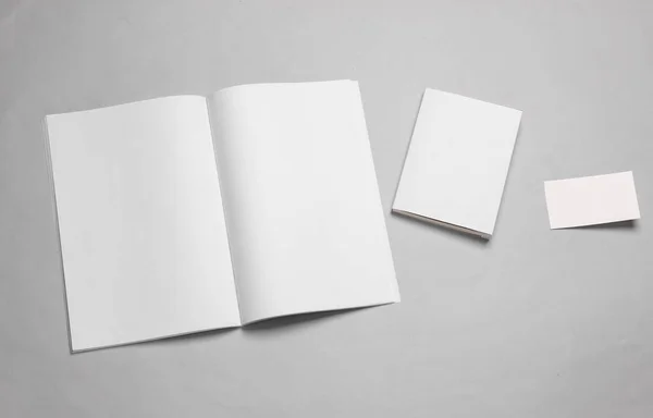 Template for design. Mockup of an open magazine or notebook with white pages, a book with an empty cover and a business card on a gray background. Flat lay