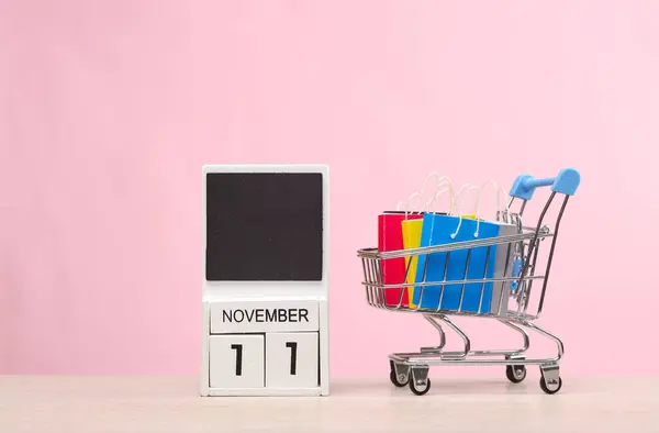 Mini Supermarket cart with shopping bags and calendar with the date november 11 on the table, pink background. World Shopping Day. 11.11.