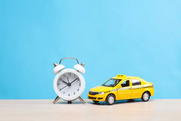 Miniature taxi car with alarm clock on table, blue background