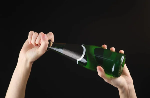 黒い背景に緑のアイルランドのビールのボトルを保持する女性の手 — ストック写真