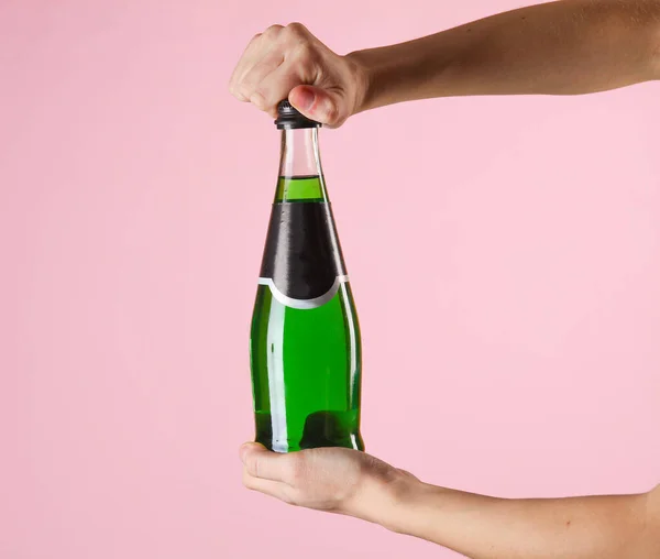 Female hands open bottle of green Irish beer on pink background