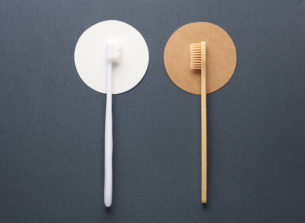 Plastic and wooden toothbrushes on dark background with circles. Eco concept. Top view.