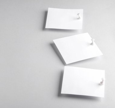 Gri zemin üzerinde raptiye olan beyaz, boş not kağıtları. Tasarım şablonu.