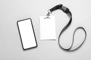 Beyaz ekranlı akıllı telefon ve gri arka planda boş beyaz kimlik kartı modeli. Personel kimlik kartı. Metin ve tasarım için boşluk.