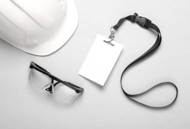 Üzerinde koruyucu miğfer ve gri arka planda koruyucu gözlük olan boş bir beyaz kimlik kartı. Mühendis, çalışma konsepti. Çalışanların kimlikleri. Üst görünüm