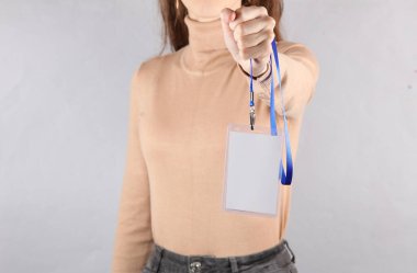 Gri arkaplanda beyaz kimlik kartı tutan genç bir kadın.