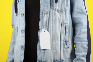 Sarı arka planda giyinmiş bir kadının kot ceketinde beyaz boş fiyat etiketi