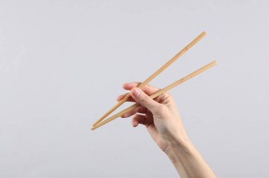Gri bir arka planda bir kadın elinde Çin yemek çubukları.