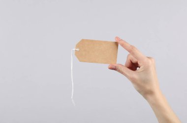 Kadın el, gri arka planda boş fiyat etiketi tutuyor. Satış konsepti