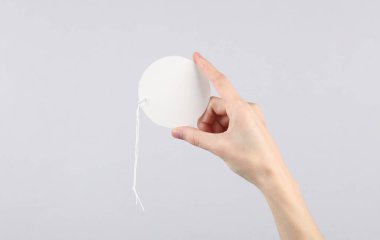 Kadın eli gri arka planda beyaz, boş, yuvarlak fiyat etiketi tutuyor. Satış konsepti