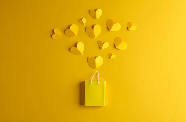 Miniature shopping bag with hearts on a yellow background. Sale, love, shopping concept. Creative layout