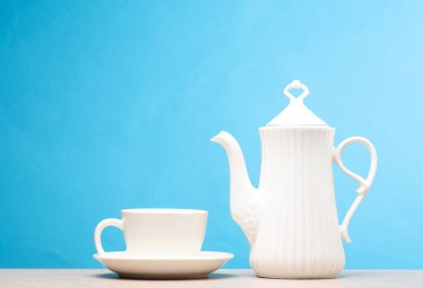 Masanın üzerinde mavi bir fincanla beyaz seramik çaydanlık. Çay töreni.