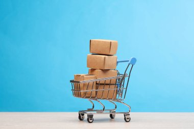Mavi arka planda karton kutuları olan süpermarket arabası..