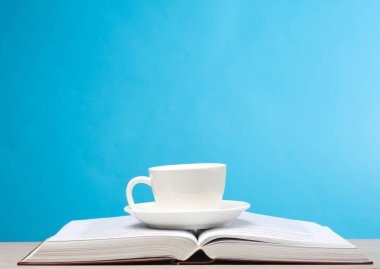 Masanın üzerinde kahve fincanı olan açık bir kitap, mavi arka plan.