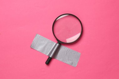 Pembe arka planda yapıştırıcı bantla tutturulmuş büyüteç. Kavramsal pop, çağdaş sanat, minimalist natüralist hayat