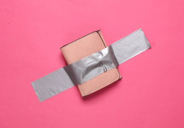 Pembe arka planda yapışkan bantla sabitlenmiş deri çanta. Kavramsal pop, çağdaş sanat, minimalist natüralist hayat