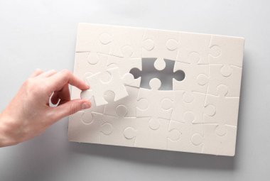 Kadın eli, gri arka planda beyaz bir yapboz oluşturur.