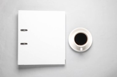Gri arka planda kahve fincanı olan beyaz klasör. Üst görünüm