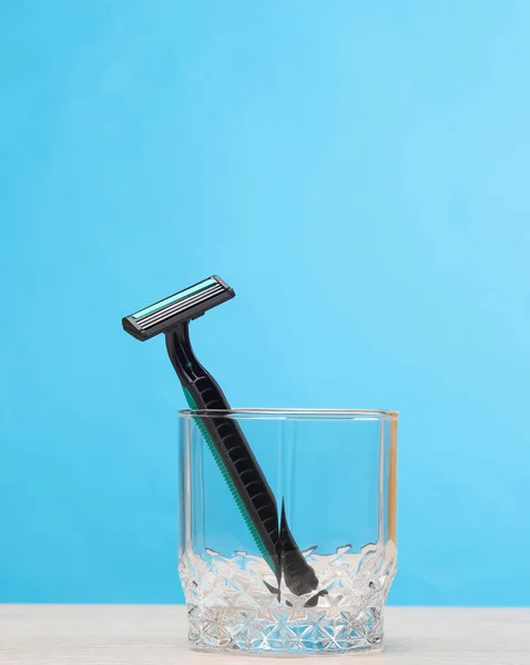 Disposable razor in a glass on the table, blue background