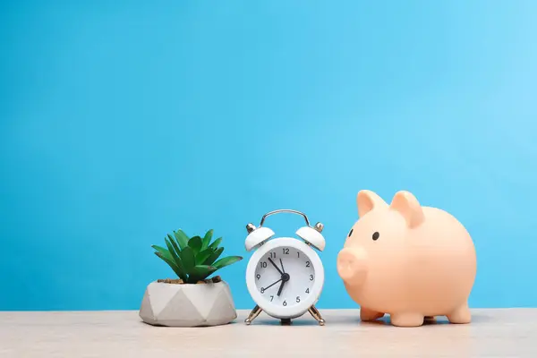 Piggy bank with an alarm clock and a plant on a blue background. Time is money, business concept