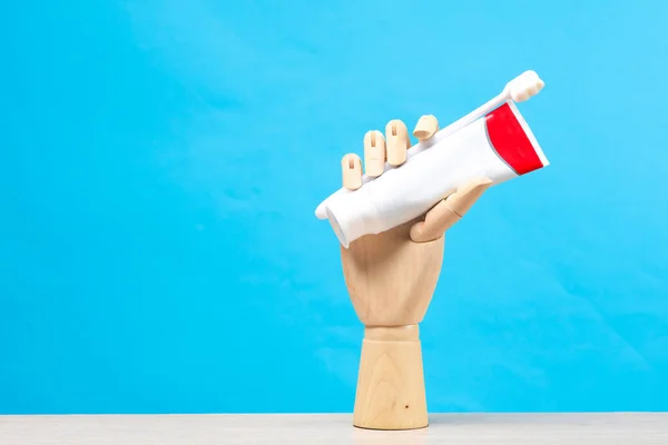 Wooden puppet hand holding a toothbrush with a tube of paste on a blue background
