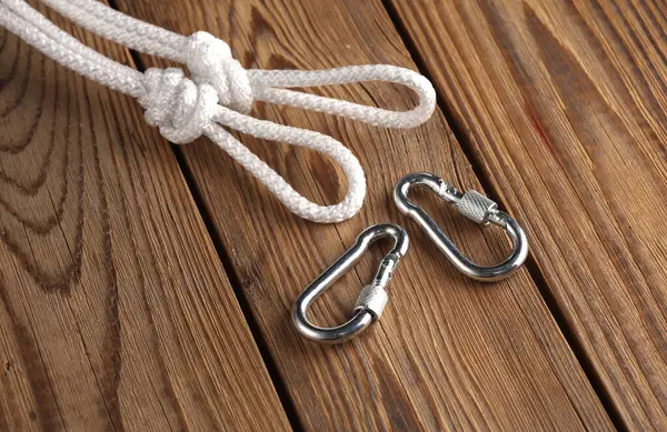 Rope with knots, loops and carabiners on wooden background. Safety rope, climbing equipment