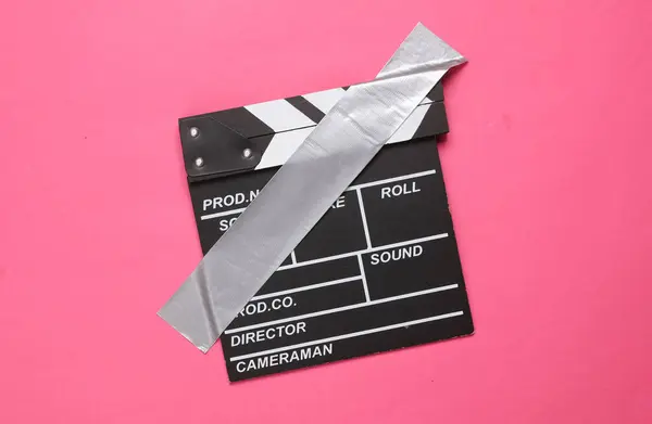Movie clapperboard fixed with adhesive tape on a pink background. Conceptual pop, contemporary art, minimalist still life