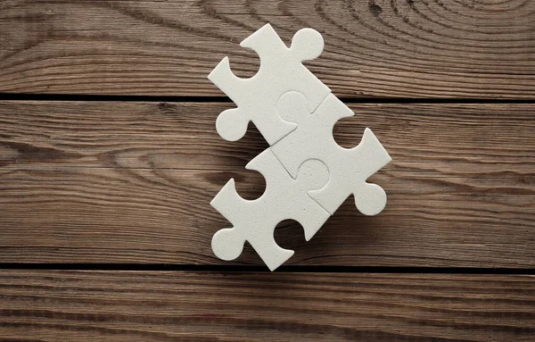 White jigsaw puzzle pieces on wooden background.