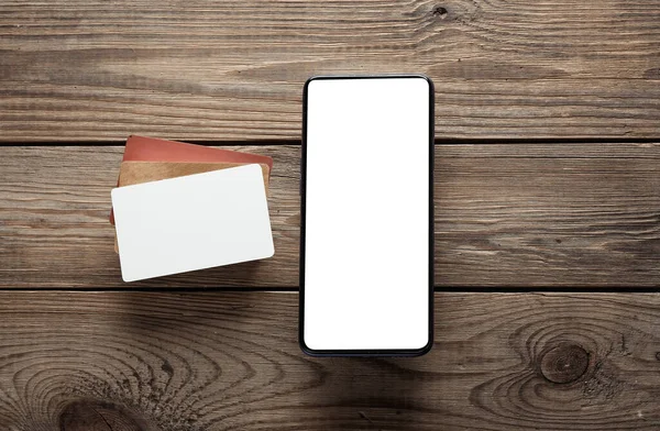 Mockup of white blank bank card and blank screen smartphone on wooden table. Template for design